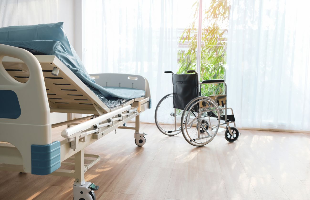 Ein Krankenhausbett mit einem Rollstuhl davor, der für die Mobilität von Patienten bereitsteht.