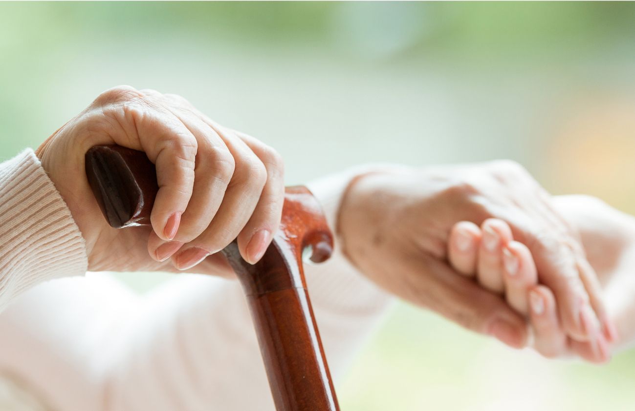 Zwei Frauen, eine mit einem Stock, halten sich an den Händen und zeigen gegenseitige Unterstützung und Verbundenheit.