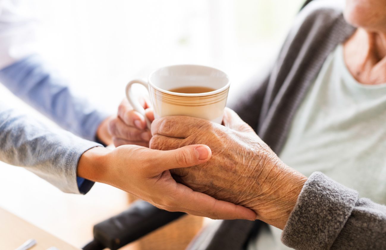 Eine Krankenschwester reicht einer älteren Frau eine Tasse Kaffee und zeigt Fürsorge und Unterstützung in der Pflege.