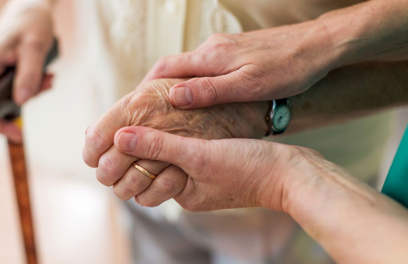 Eine ältere Dame greift nach der Hand einer jüngeren Frau, was die enge Bindung und Unterstützung zwischen den Generationen zeigt.
